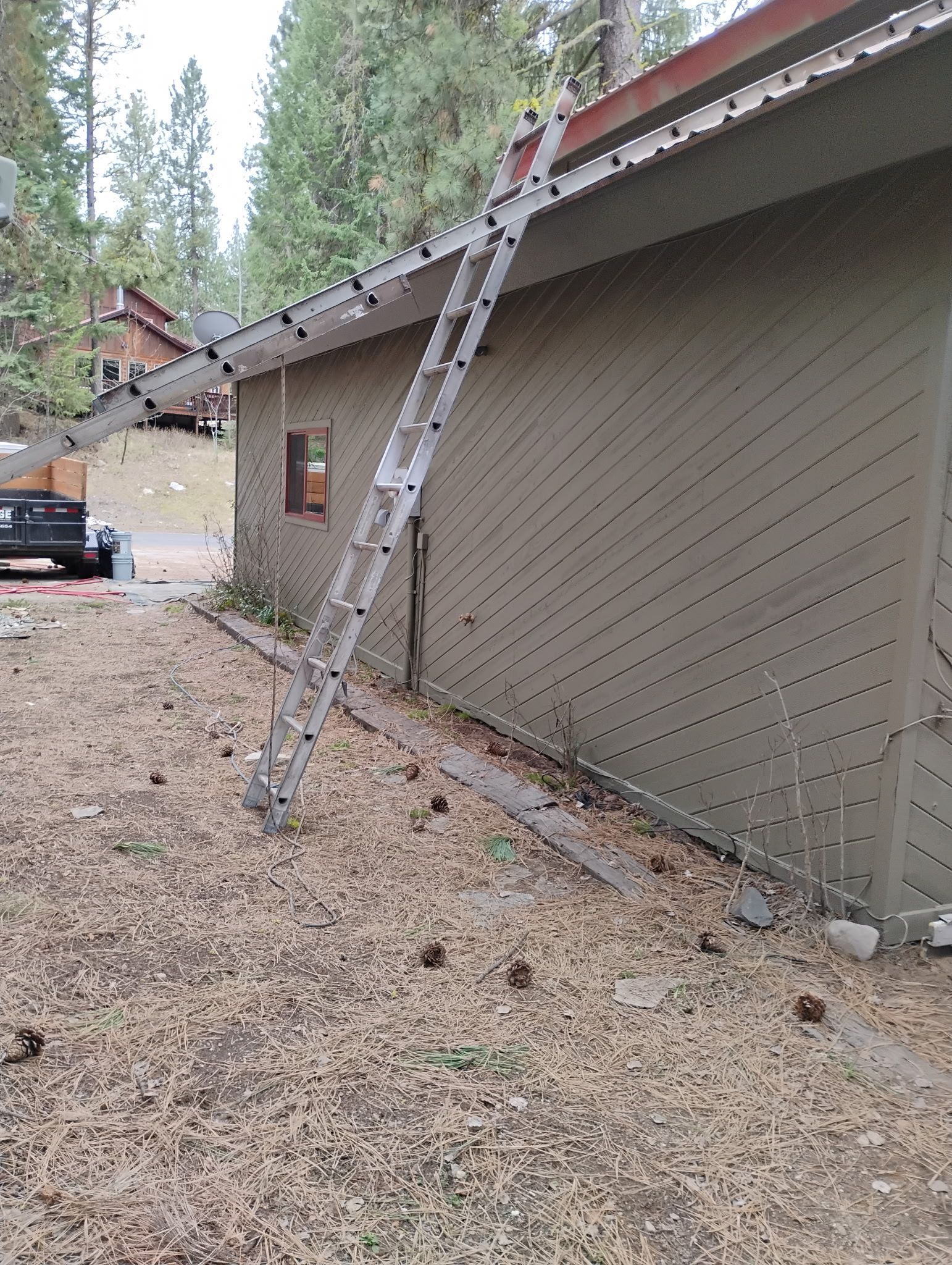 Damaged roof with a ladder leaning against a beige house in a wooded area