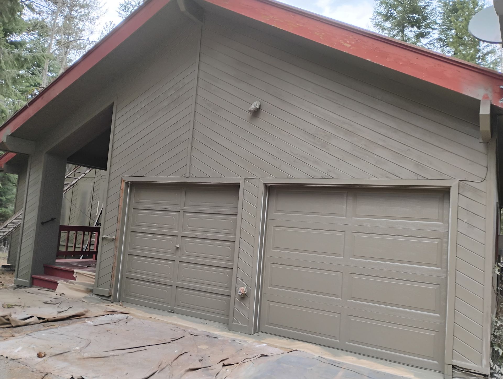 Two-car garage with beige doors and red-trimmed roof on a gray house