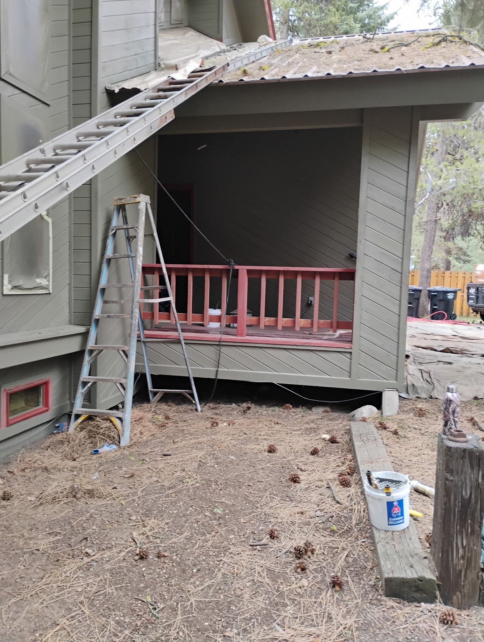 Ladders lean against a house with fire damage, exposing a charred porch and roof under repair.