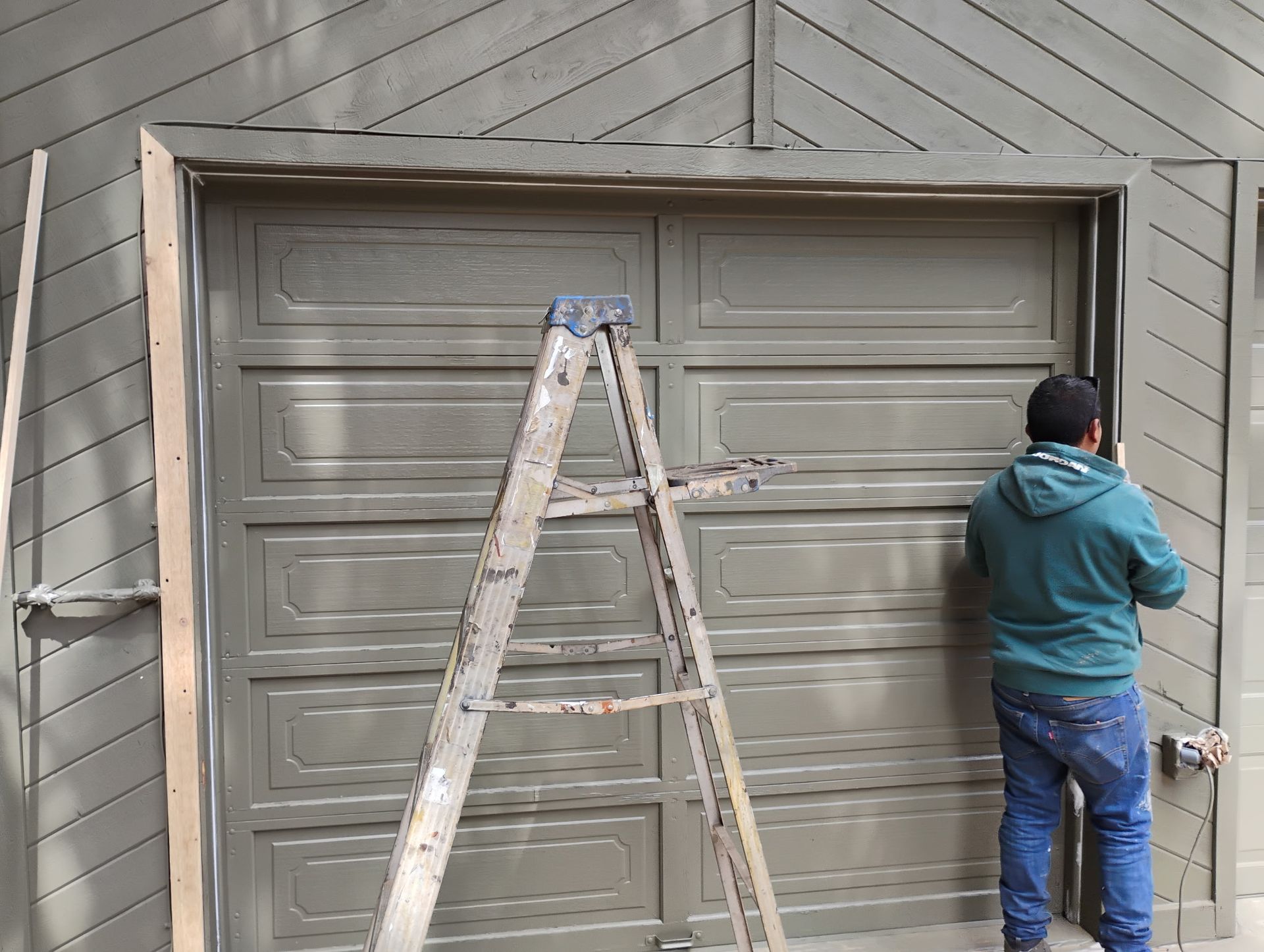 Person standing by a garage door, with a ladder centered in front of it.