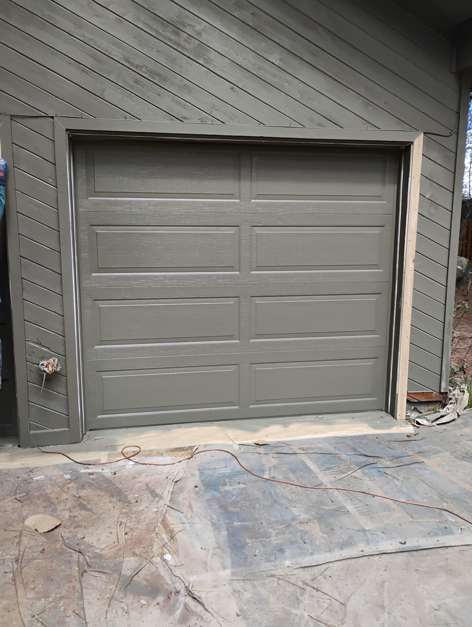 Gray garage door set into a striped exterior wall with a concrete driveway in front