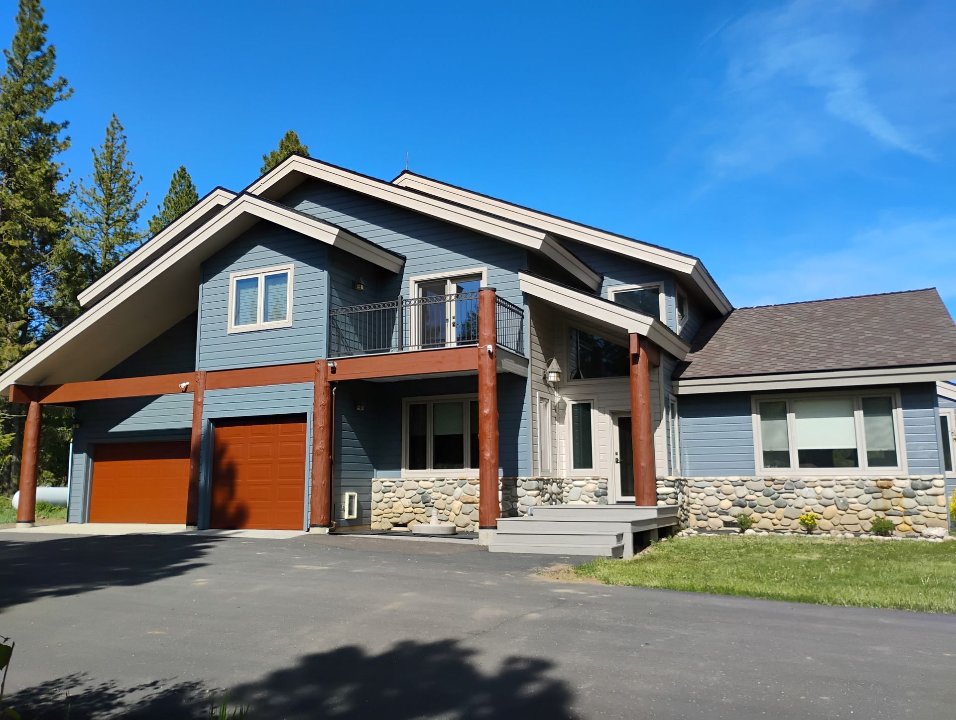 Large modern house with gray siding, stone accents, and red garage doors under a blue sky