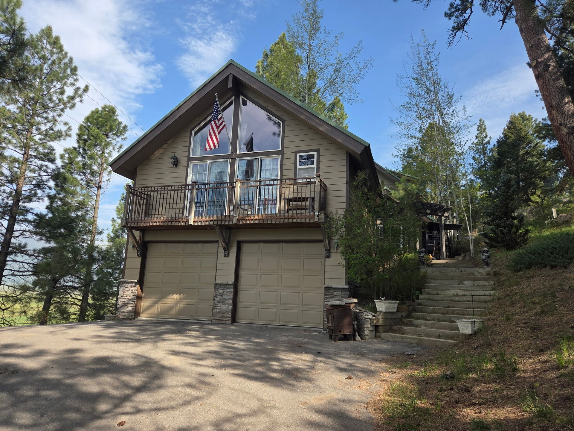 Cabin-style house with balcony, garage, and stone steps among tall pine trees