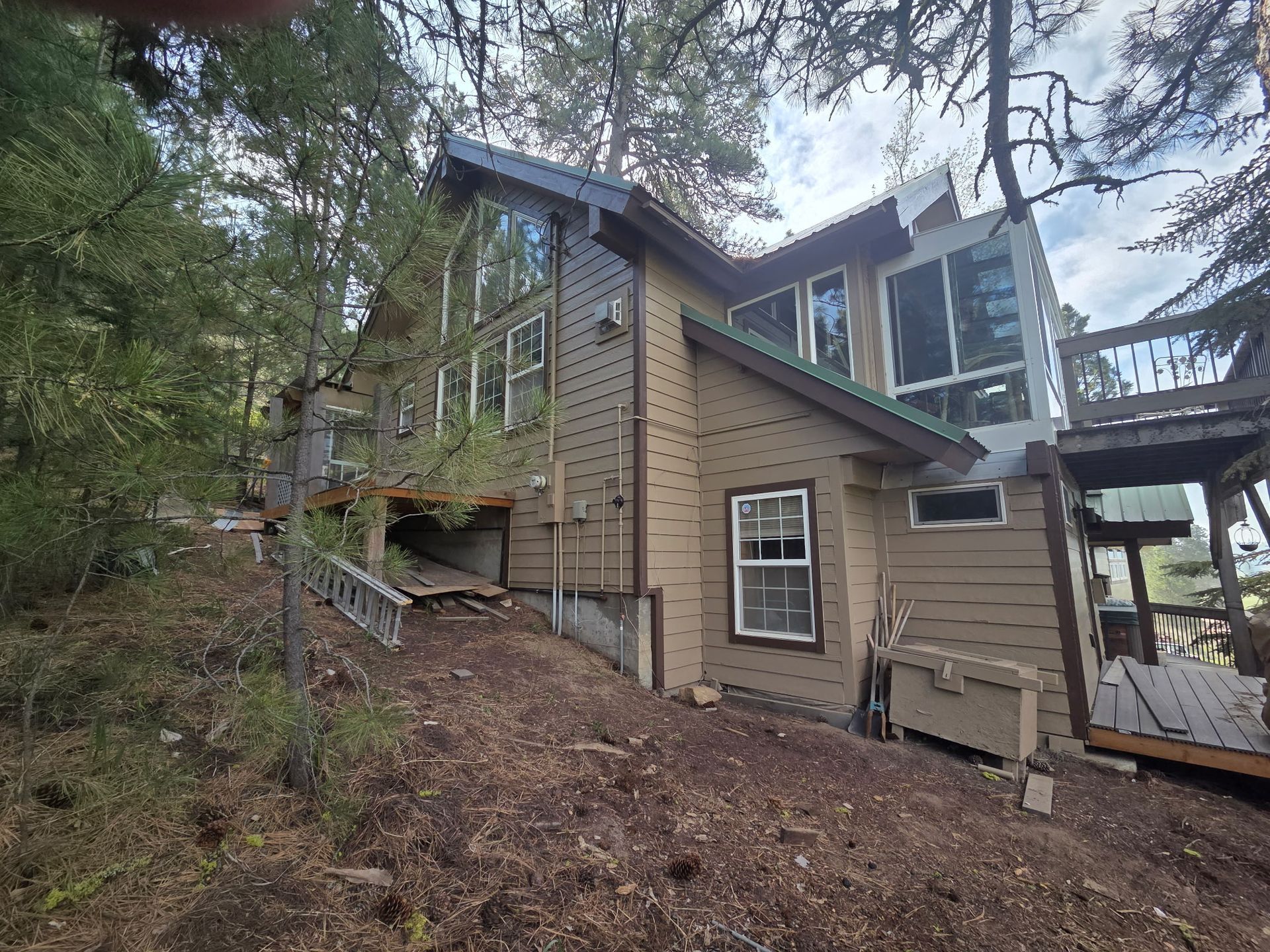 Wooded hillside home with tan siding, large windows, and a covered deck