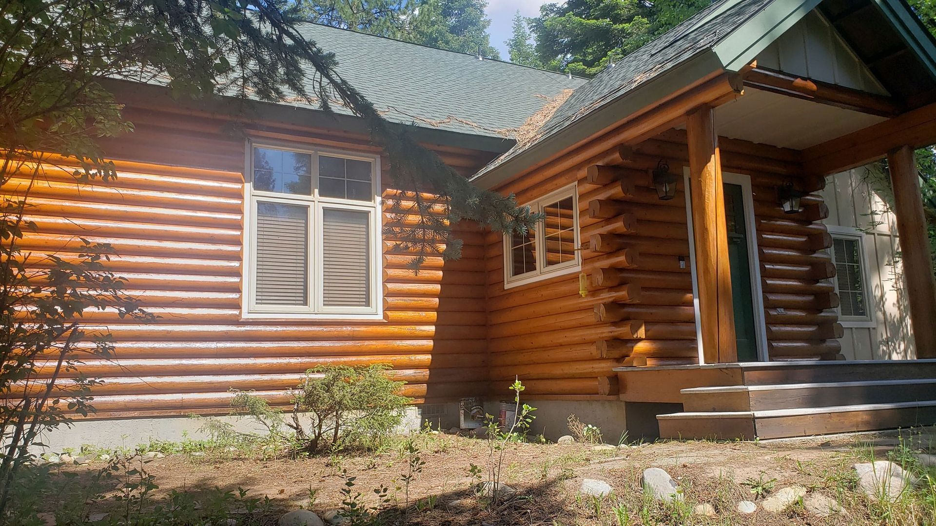 A log cabin with a porch and stairs in the woods.