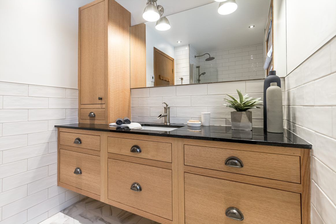 A bathroom with a sink , mirror , cabinets and drawers.