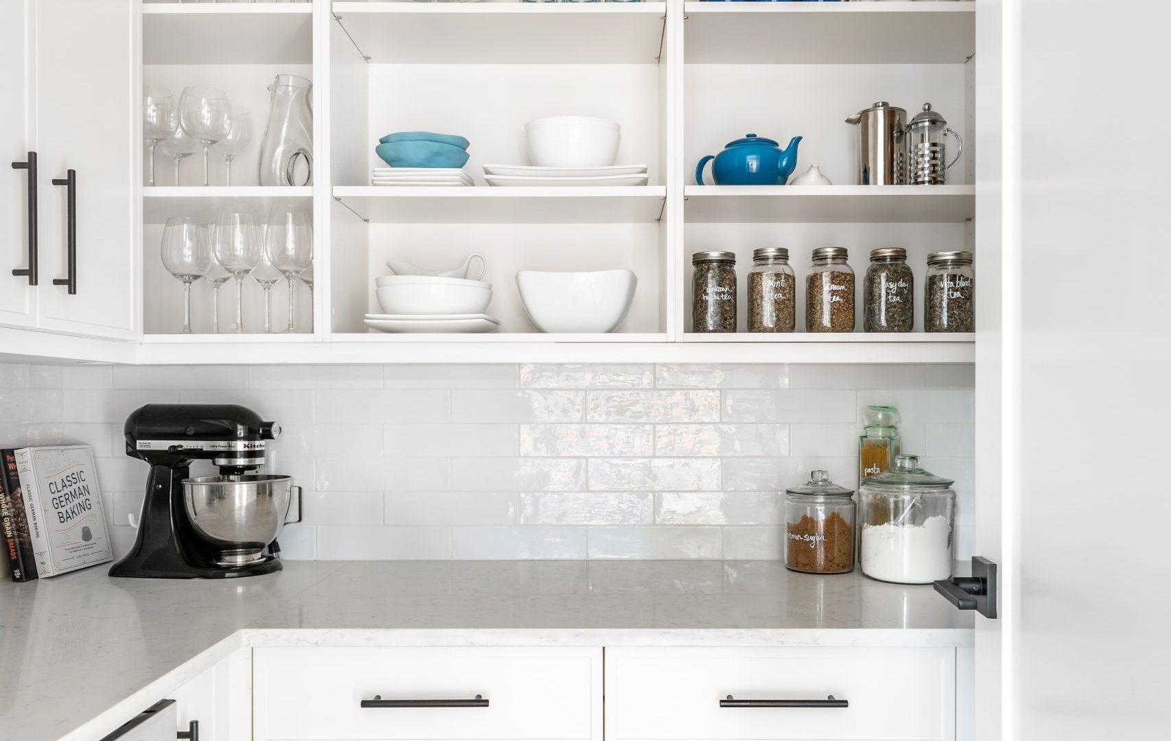 A kitchen with white cabinets , white counter tops , a mixer , and a pantry.