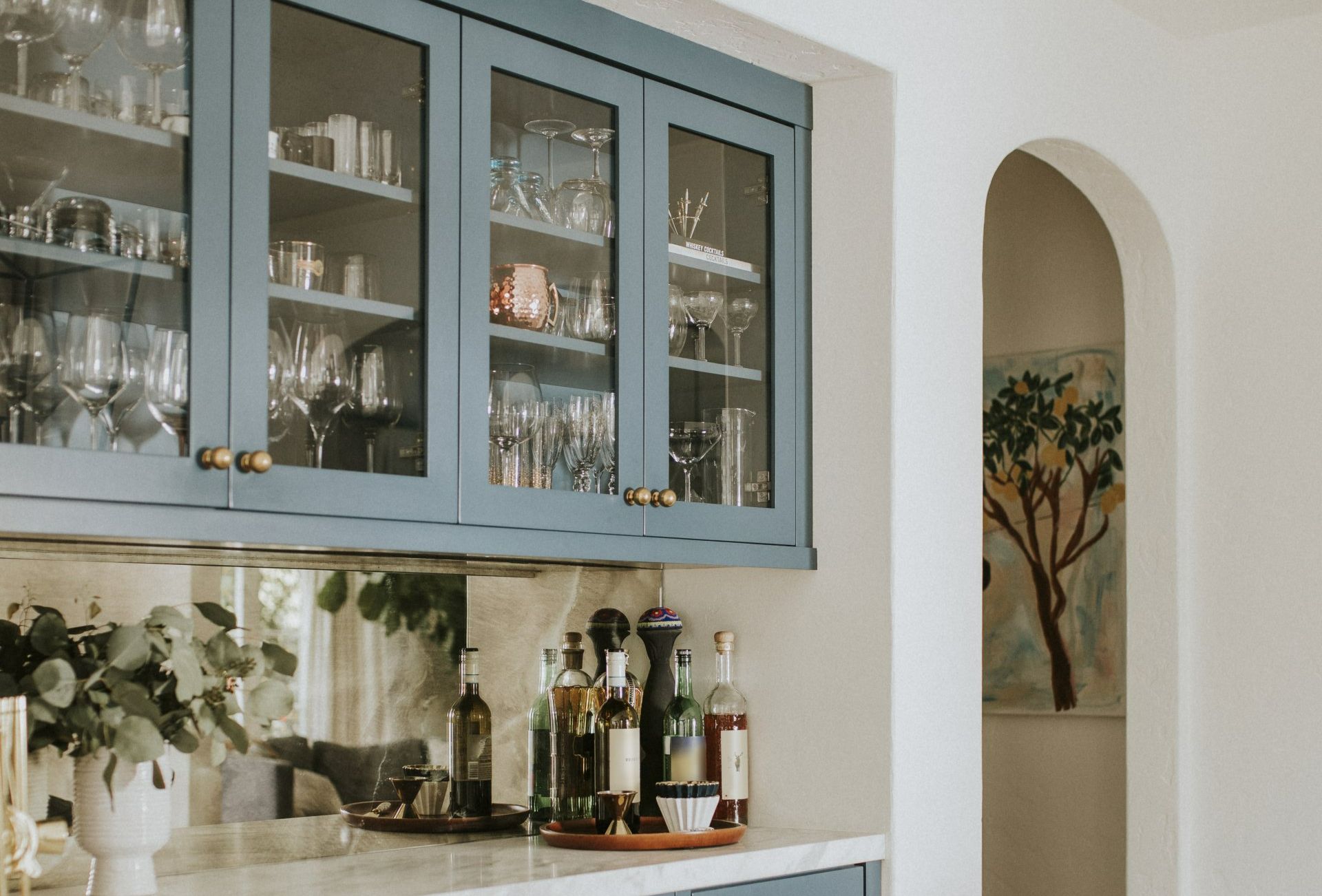 A kitchen with blue cabinets and glass doors filled with bottles and glasses.