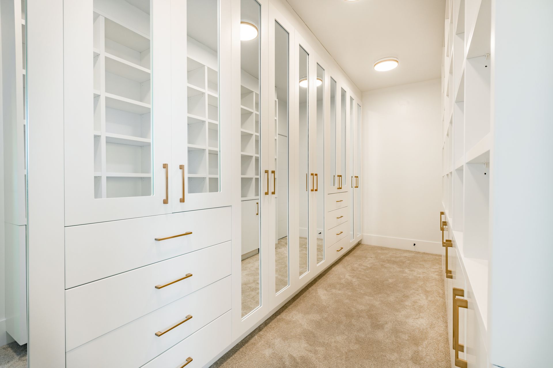 A walk in closet with white cabinets , drawers , and mirrors.