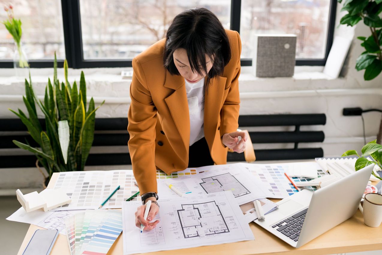 A woman is sitting at a desk looking at a blueprint of a house.