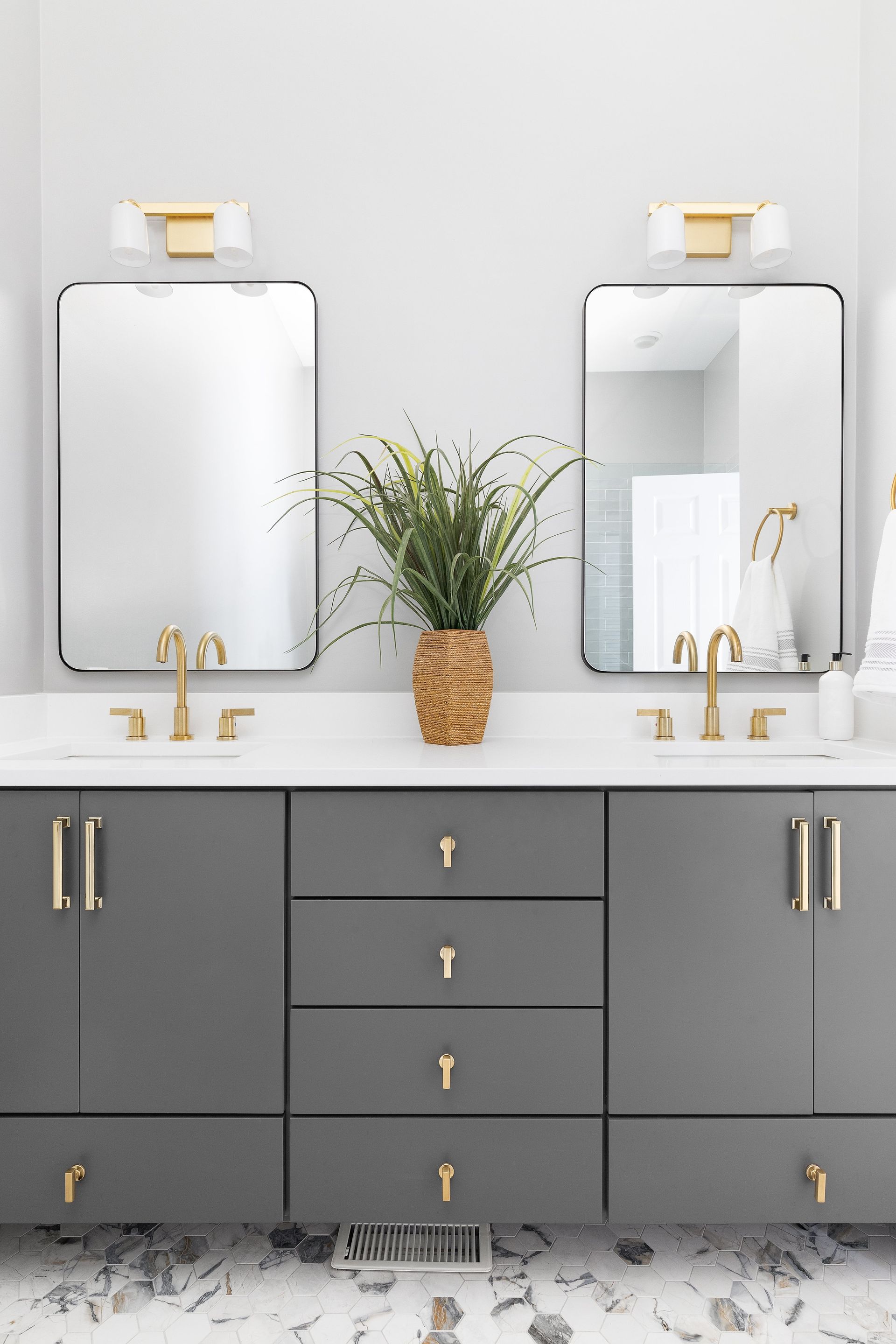 A bathroom with two sinks , two mirrors and a plant on the counter.