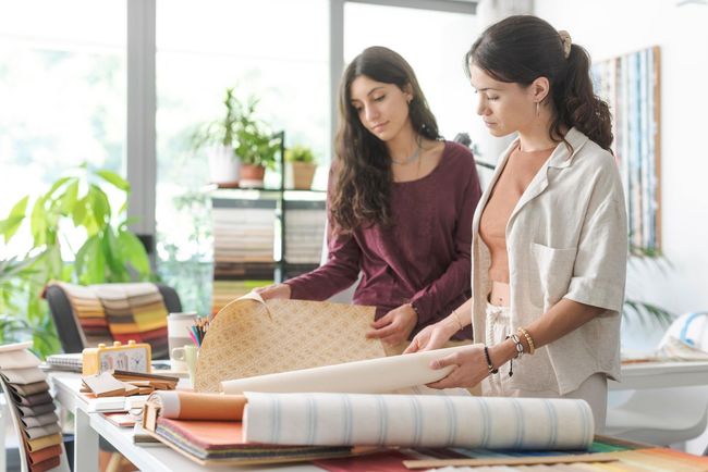 Two women are looking at rolls of wallpaper in a store.