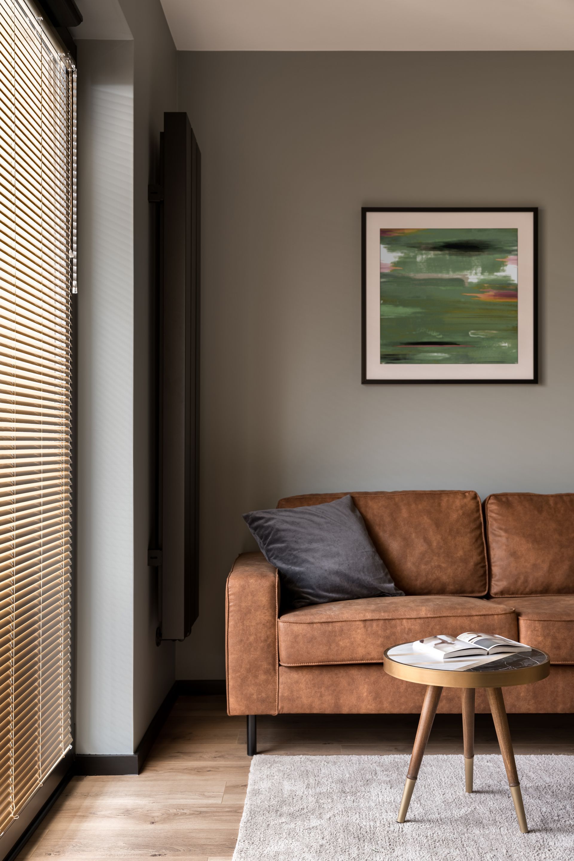 A living room with a brown couch , a table , and a painting on the wall.