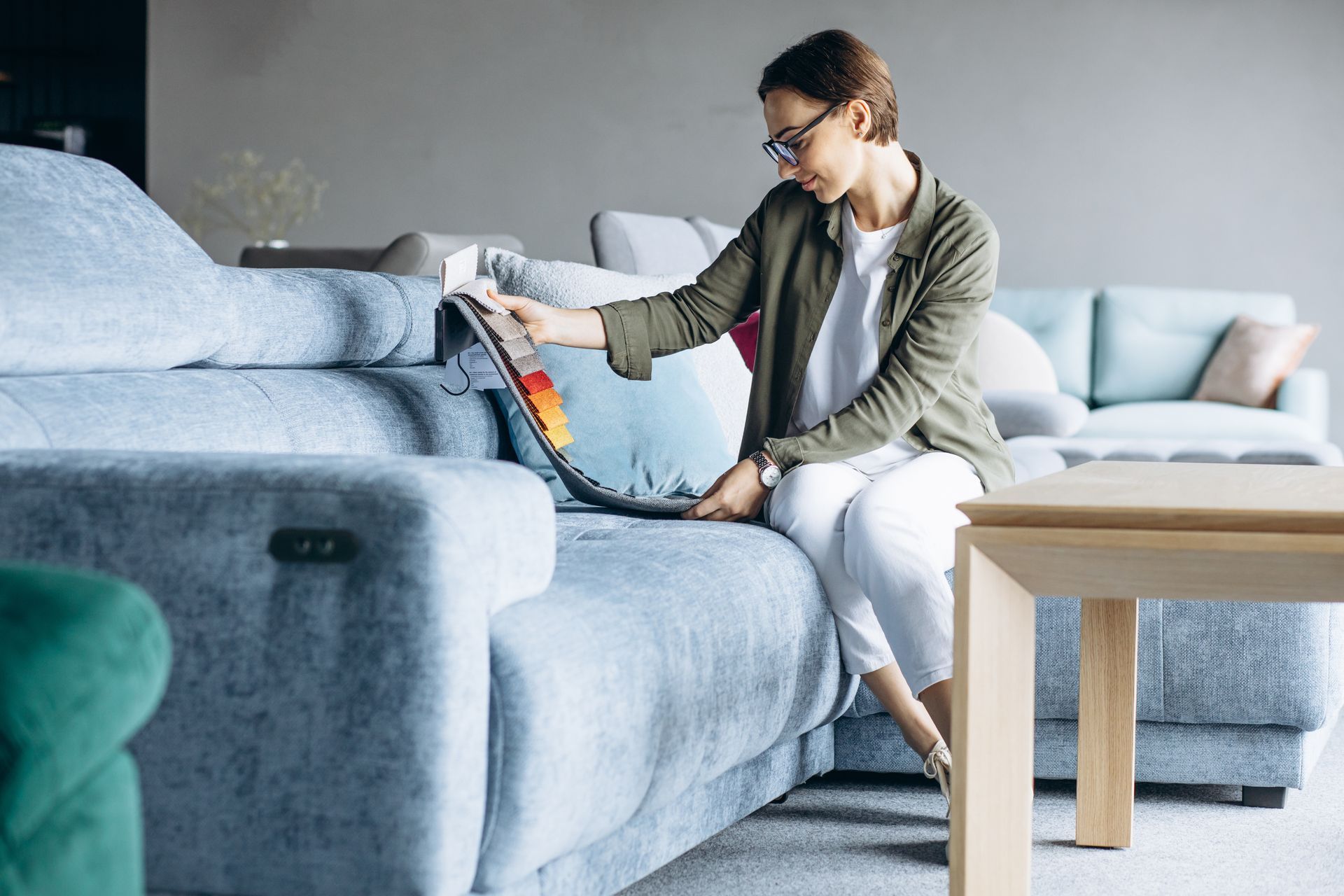 A woman is sitting on a couch in a living room looking at a pillow.