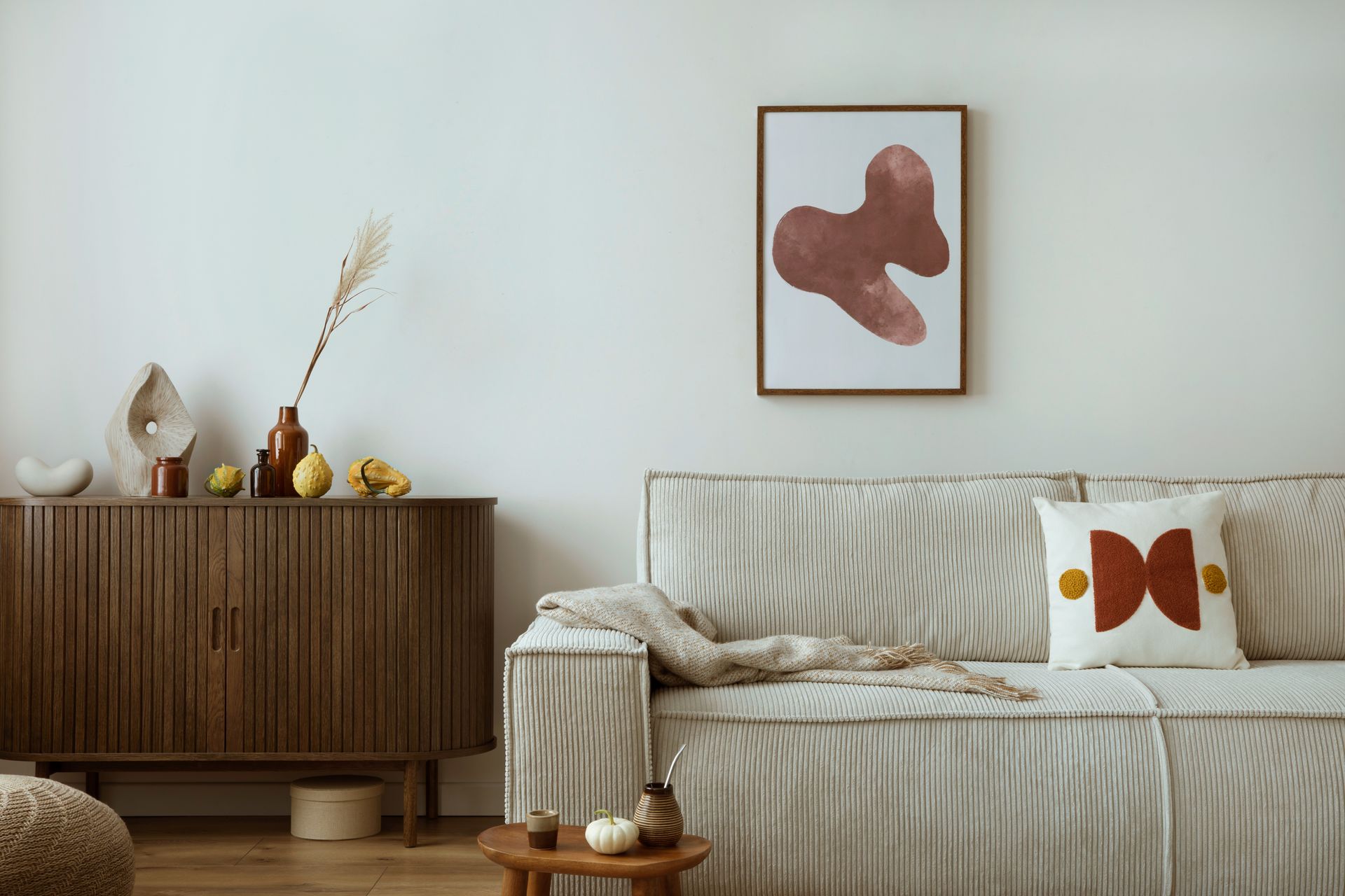 A living room with a couch , dresser , table and a painting on the wall.