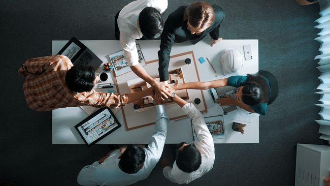 A group of people are sitting around a table shaking hands.