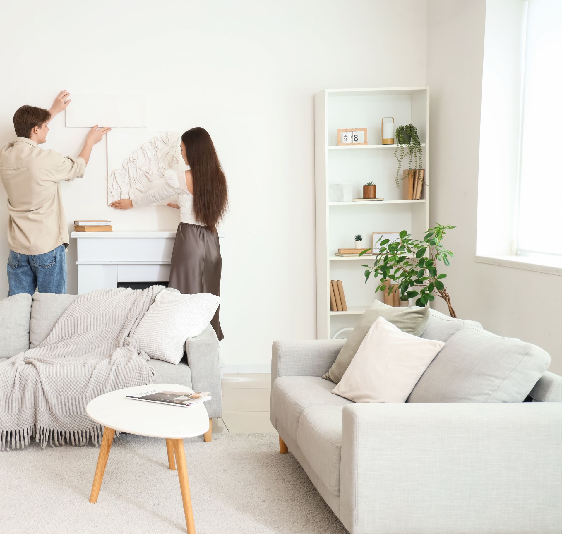 A man and a woman are hanging a picture on a wall in a living room.