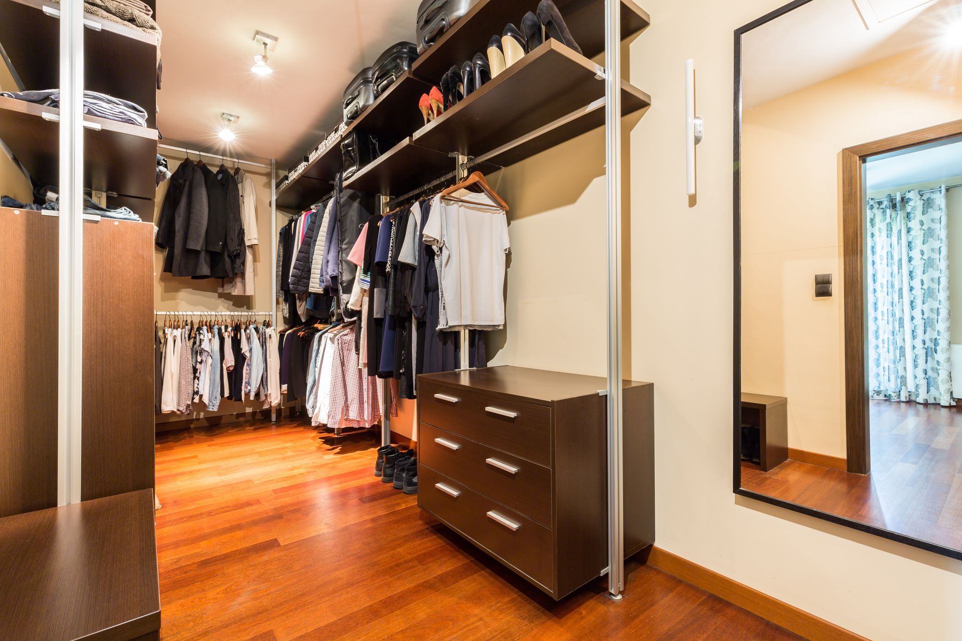 A walk in closet with lots of clothes and a mirror.