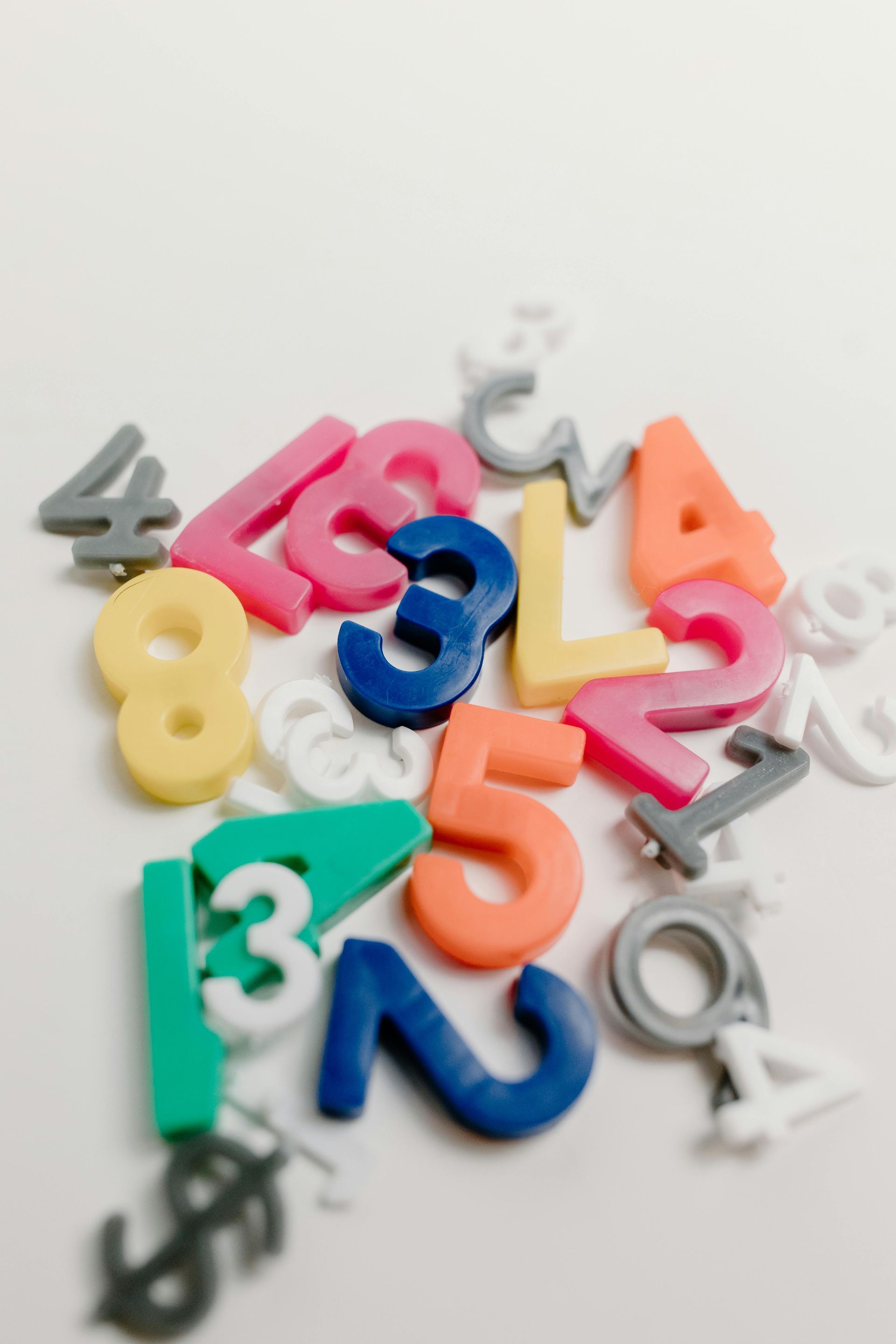 Colorful plastic numbers scattered on a white surface, various sizes, including green, pink, and blue.