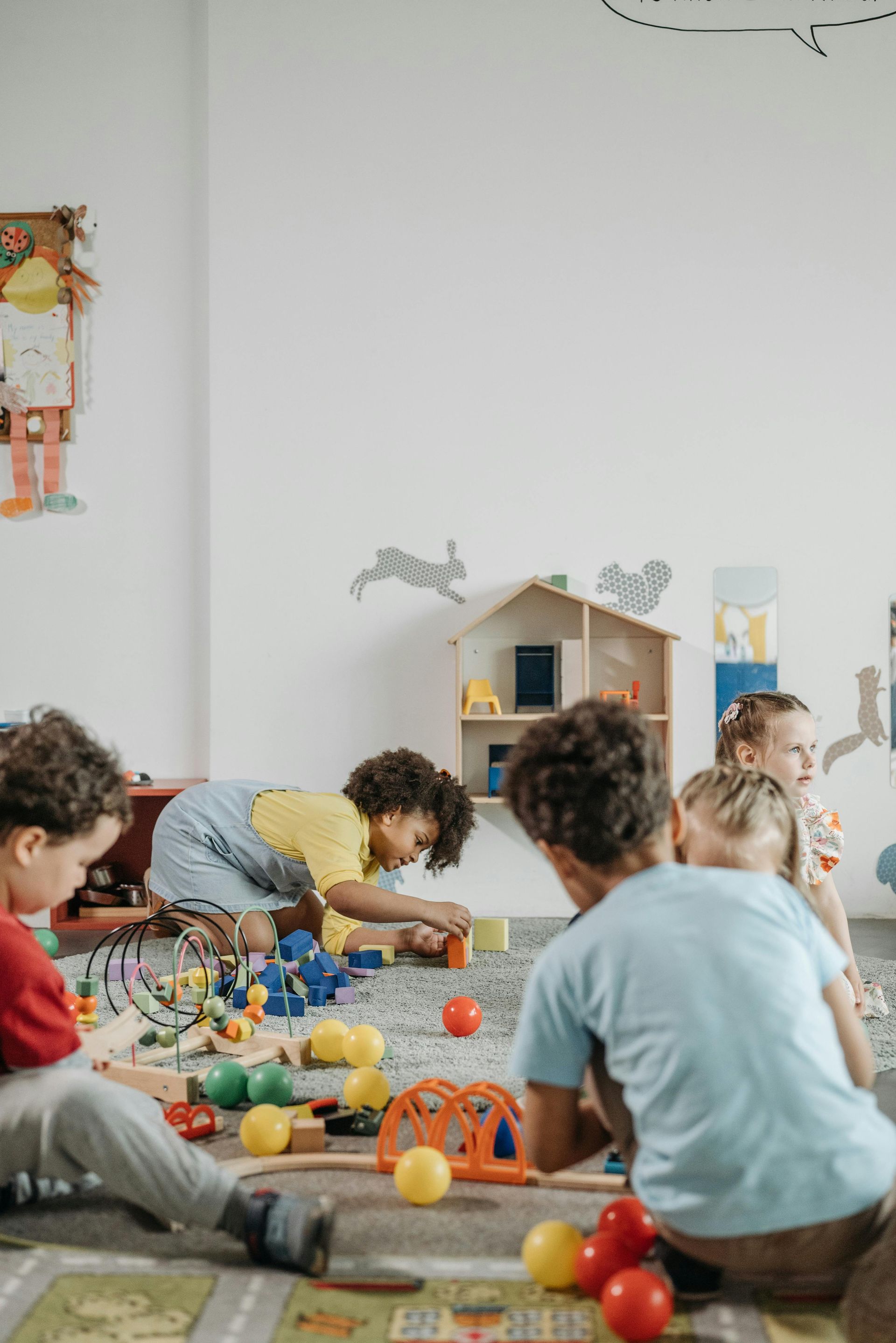 Children playing with blocks and toys on a colorful carpet in a playroom.