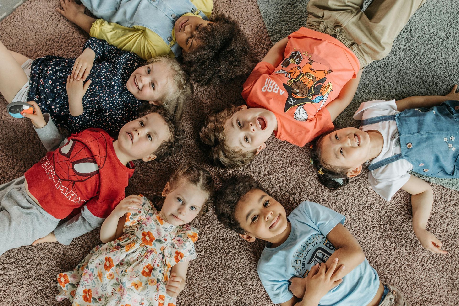 Children of diverse backgrounds lying on a carpet, looking upwards and smiling.