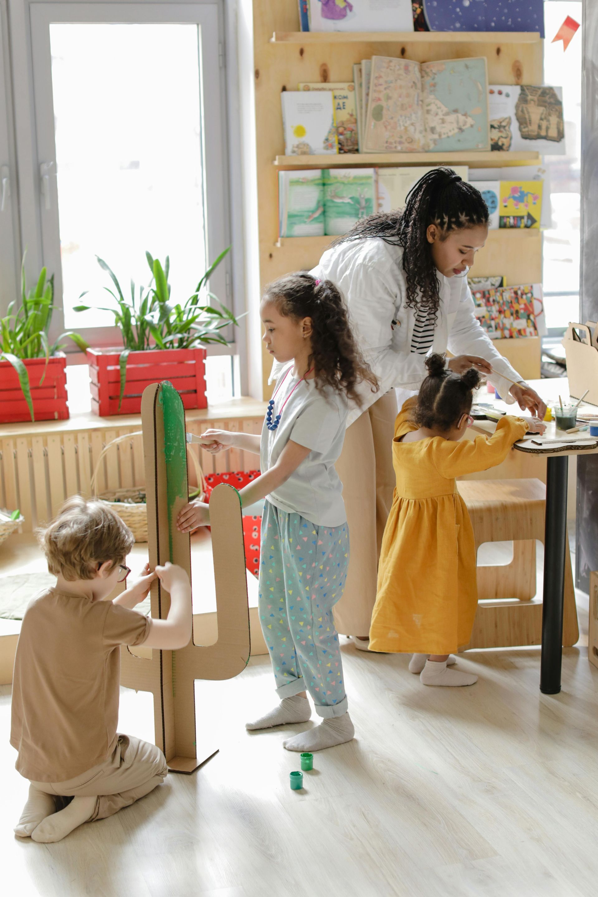 Teacher and three children arranging a cardboard cactus in a classroom.