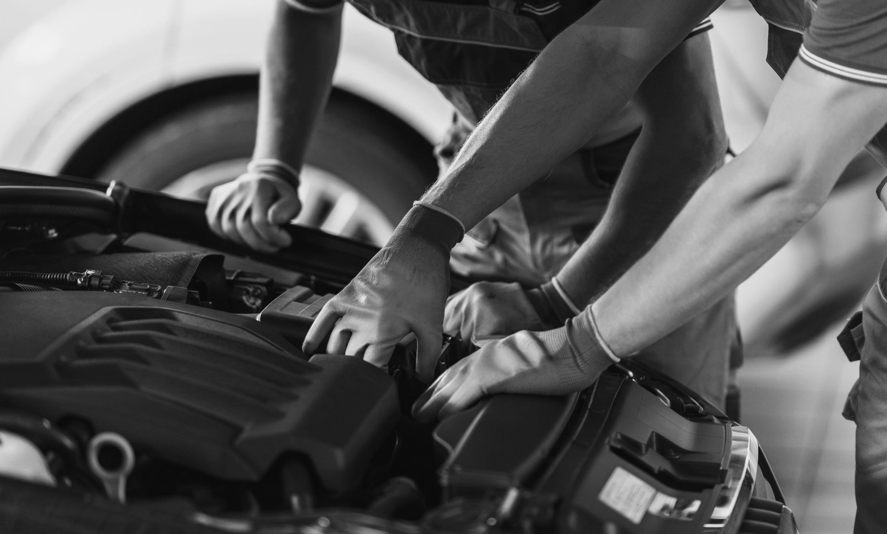 Zwei Mechaniker arbeiten mit Handschuhen an einem Automotor.
