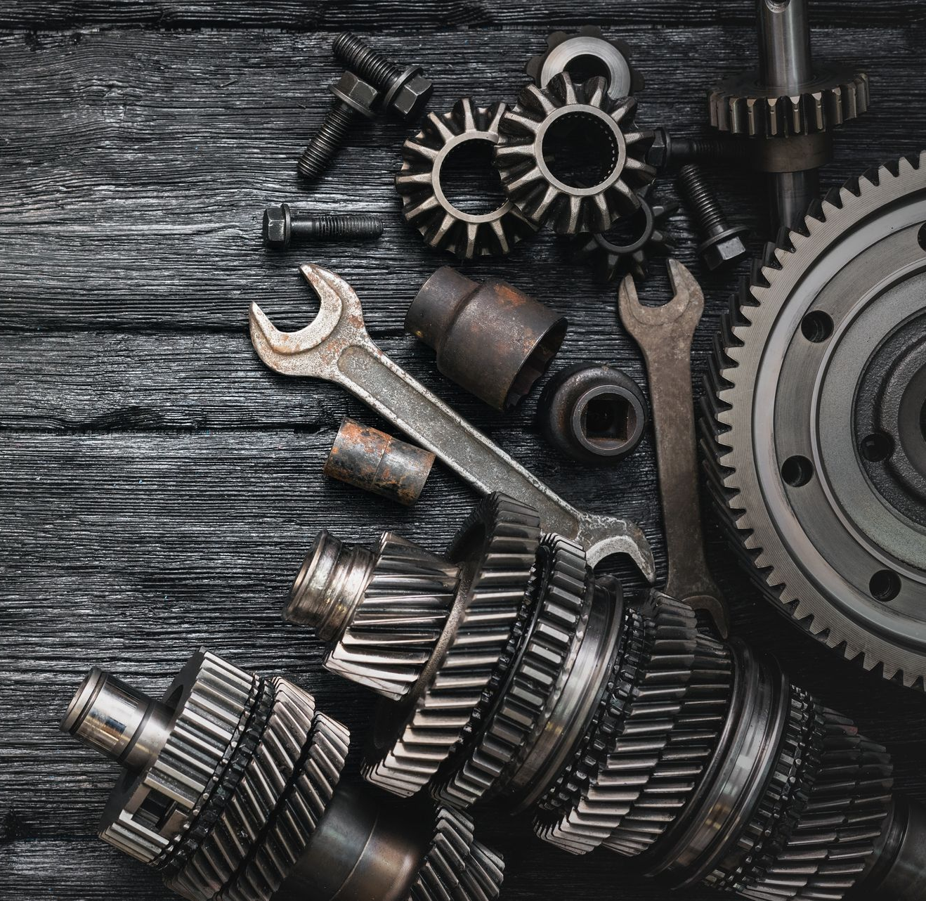 Zahnräder, Schraubenschlüssel und Bolzen auf einer strukturierten, dunklen Holzoberfläche stellen mechanische Bauteile dar.