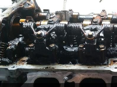 Der Zylinderkopf des Motors ist mit dickem, schwarzem Schlamm bedeckt. Ventile, Federn und Kipphebel sind sichtbar.