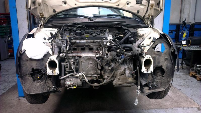 Weißer Mini Cooper, dessen Frontpartie in einer Garage demontiert ist.