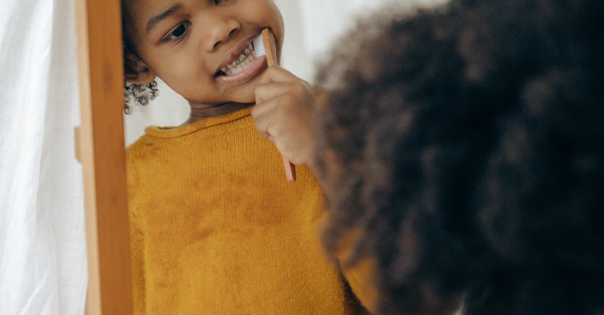A little girl is brushing her teeth in front of a mirror.