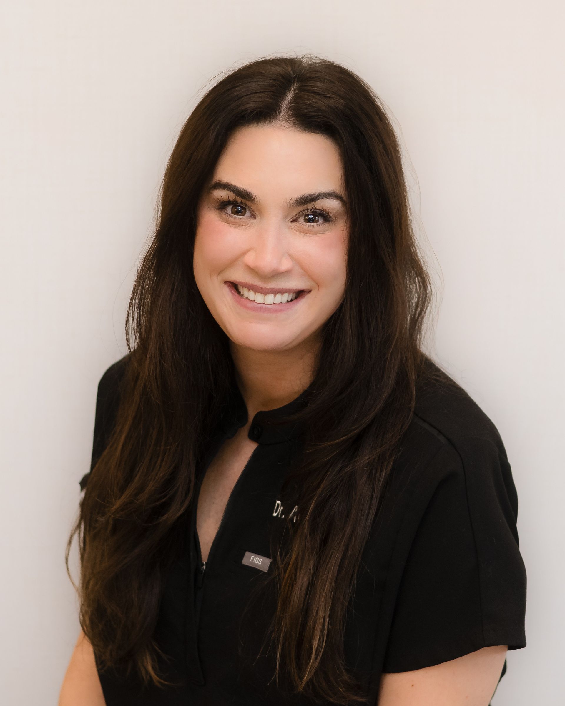 A woman with long brown hair is smiling and wearing a black shirt.