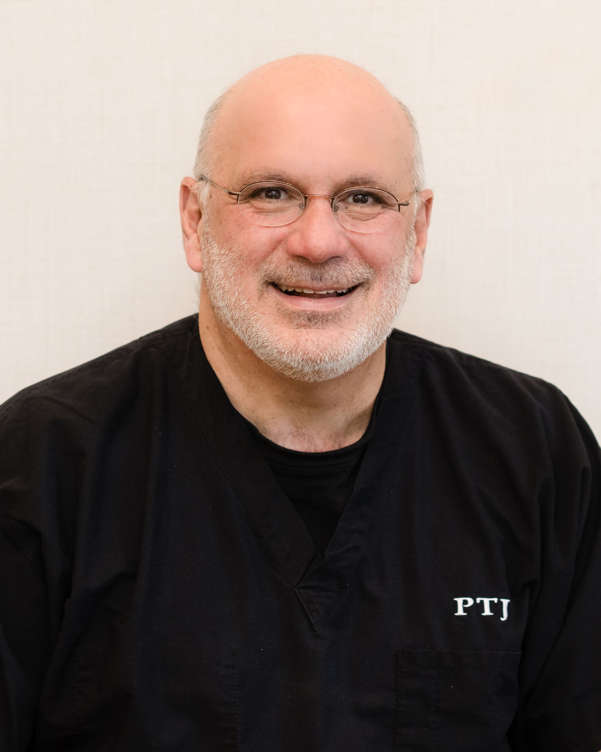 A bald man with a beard and glasses is wearing a black shirt with the word ptj on it.