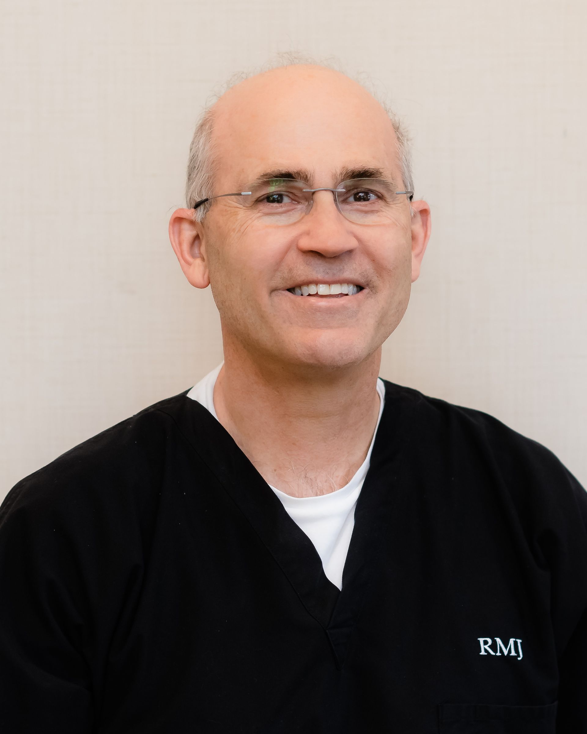 A man wearing glasses and a black scrub top is smiling for the camera.