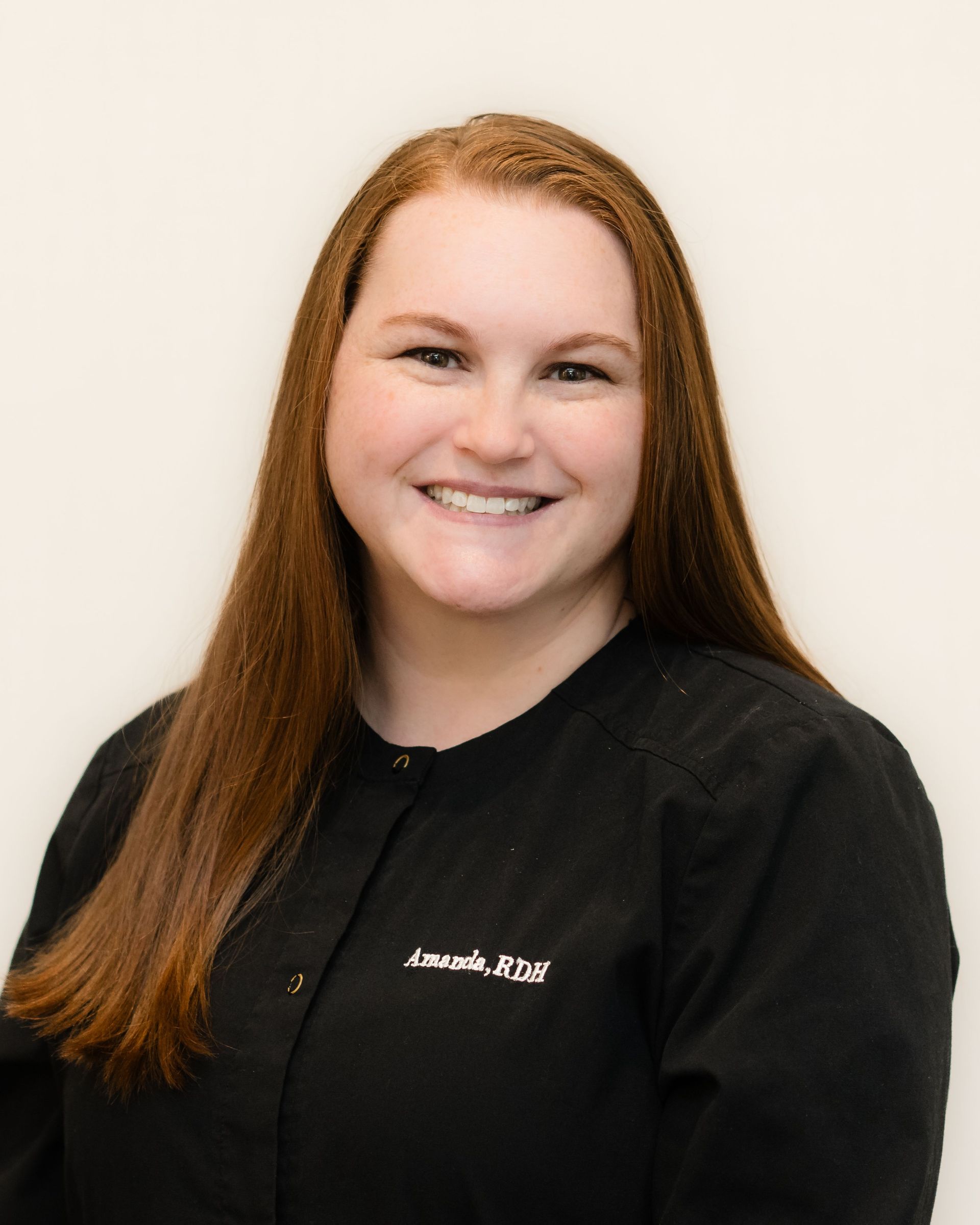 A woman with long red hair is wearing a black jacket and smiling.