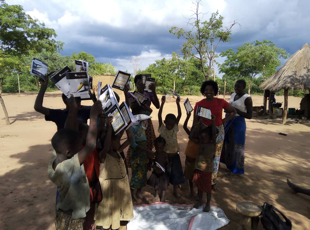 A group of people are standing in a dirt field holding papers in their hands.