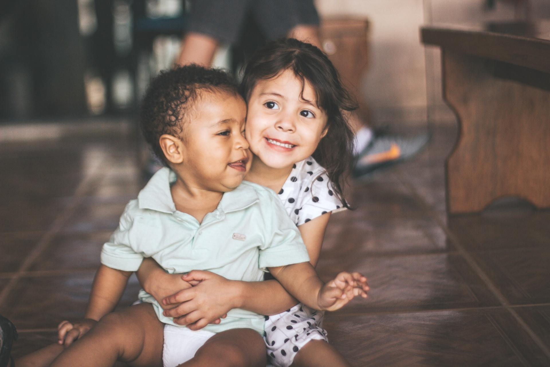 A boy and a girl are sitting on the floor hugging each other.