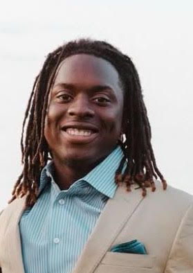 A man with dreadlocks is wearing a suit and smiling.
