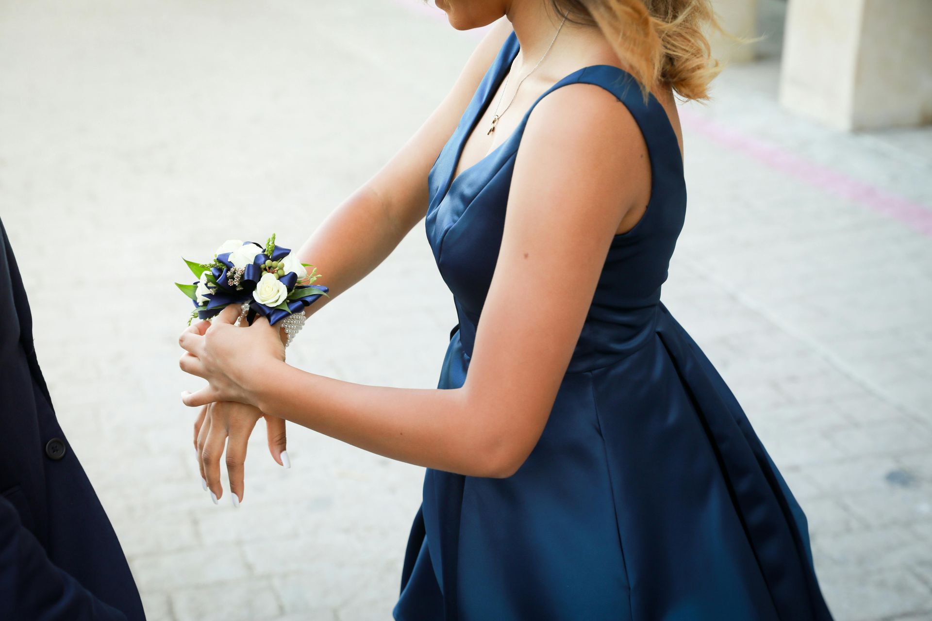 Woman in a navy dress holding a small bouquet, standing outdoors near a light stone wall.