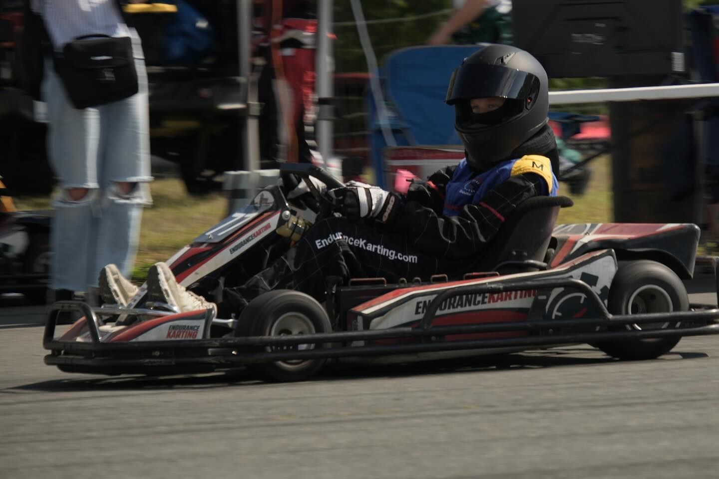Child in black helmet and suit driving a go-kart on a track.
