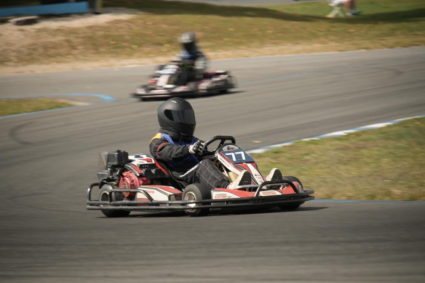 Go-kart racing on a track; driver in kart number 77 navigating a turn, another kart in background.