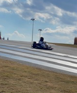 Go-kart racing on a track with white lines under a cloudy sky.