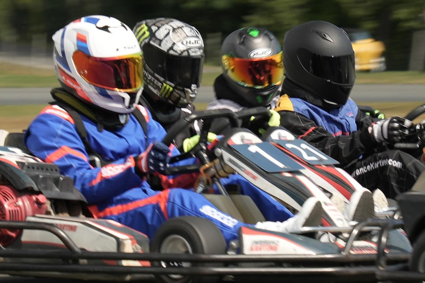 Four go-kart racers in helmets, driving on a track.