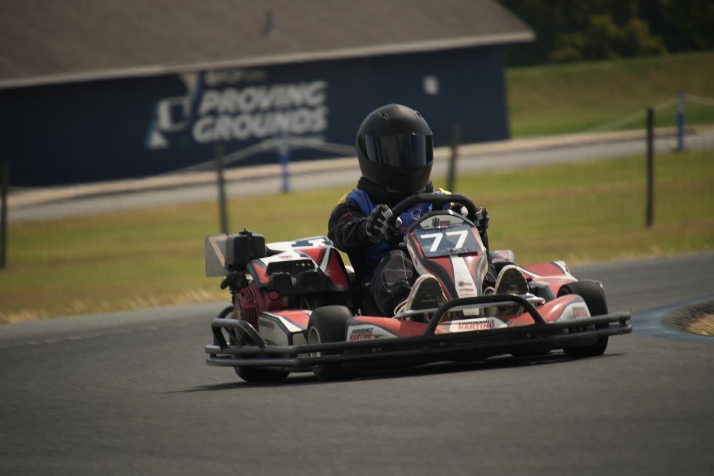 Go-kart racer in a black helmet driving on a track, number 77 on the vehicle.