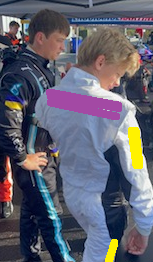 Man in black suit and young person in white suit; both outdoors near a vehicle. Pink and yellow highlights.