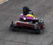 Small, toy-like vehicle with a pink and yellow car on top of a red and gray base, likely in a street setting.