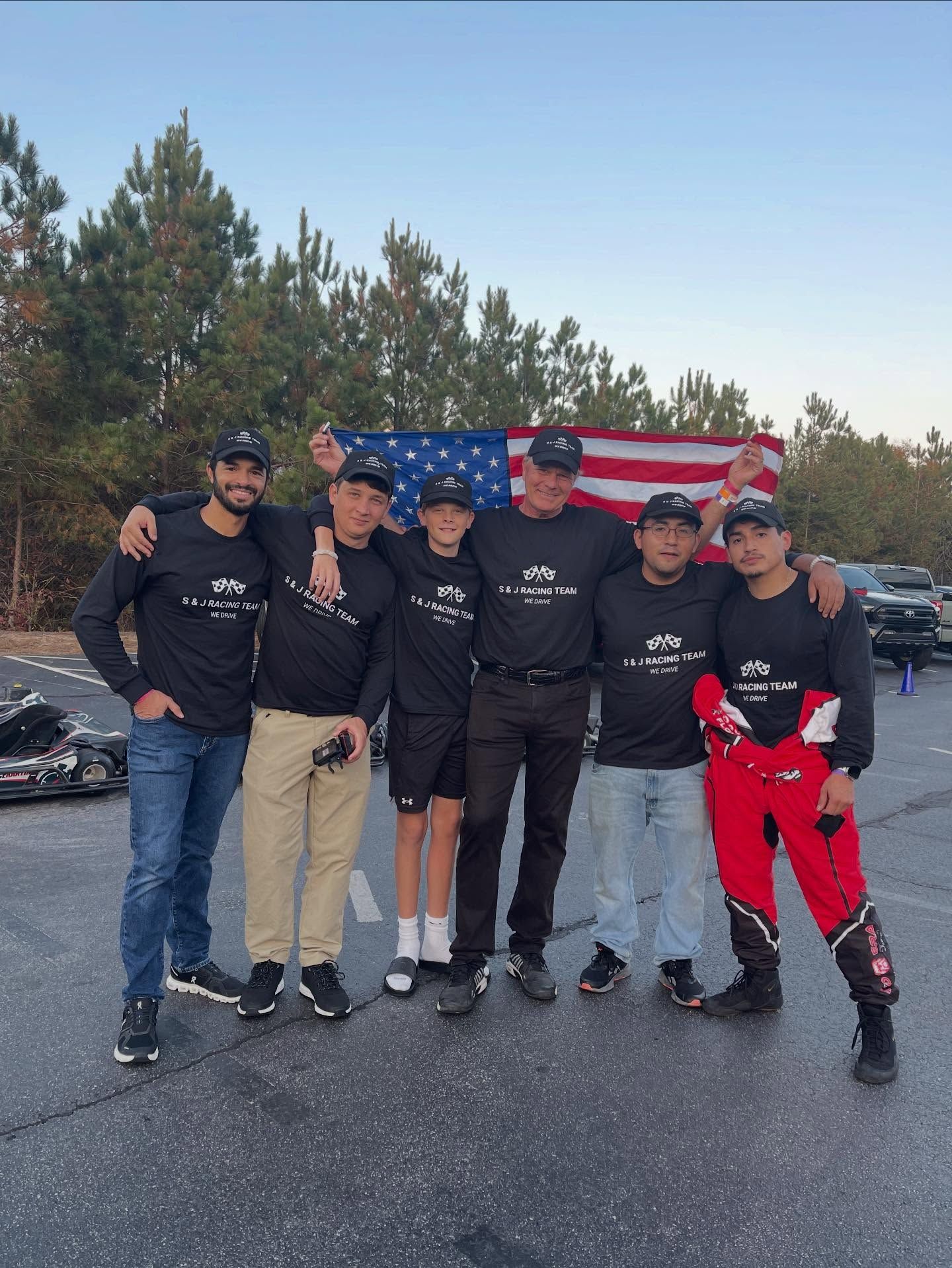 A group of people in black shirts and pants pose in front of an American flag, outdoors.