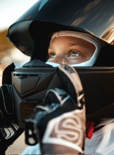 Person in a racing helmet, focused gaze upwards, holding steering wheel with gloved hands.