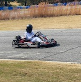 Go-kart driver in a white suit and black helmet on a race track.