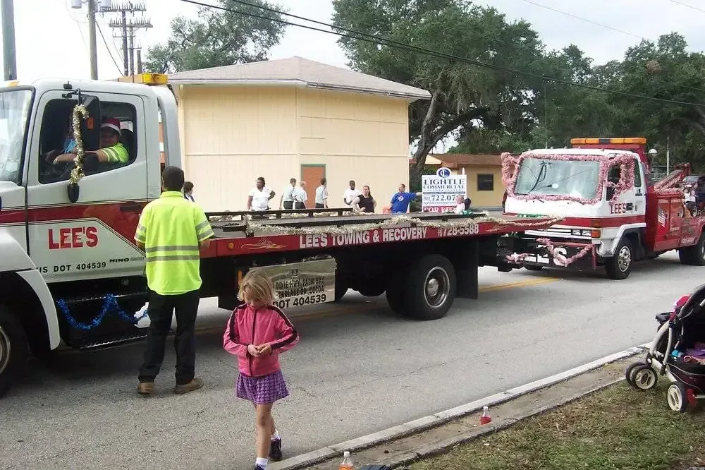 A little girl stands in front of a lees tow truck
